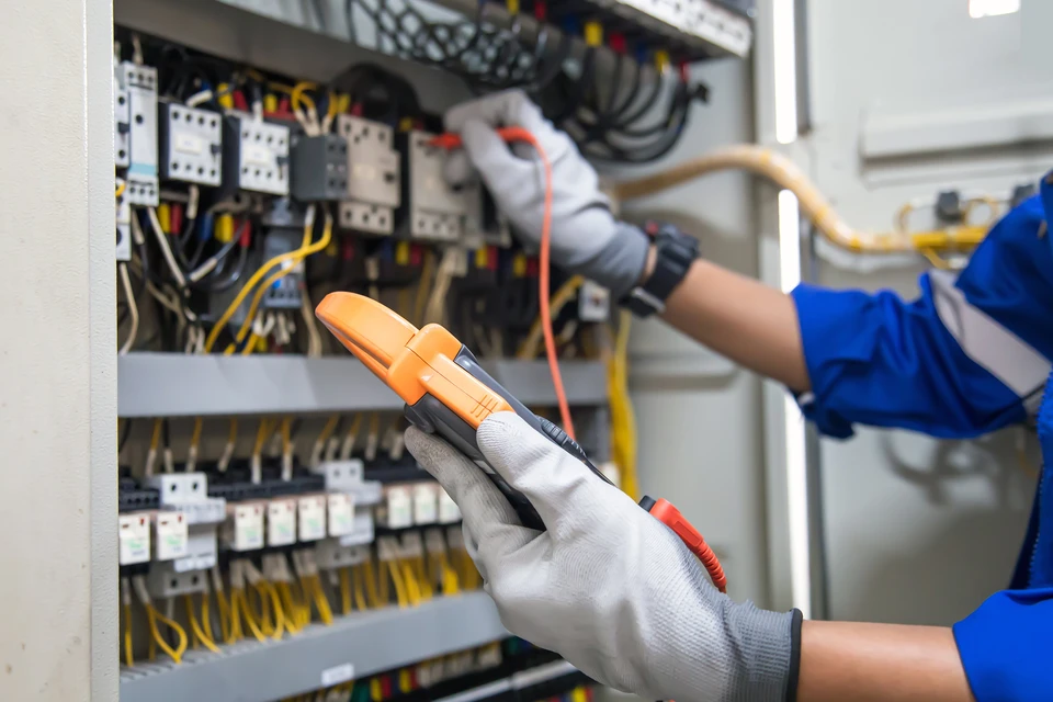 Service d'entretien de l'électricité et de l'électricité, ingénieur utilisant un outil de mesure de l'équipement pour vérifier la tension du courant électrique au terminal de disjoncteur et à la carte principale de distribution de l'énergie du câblage