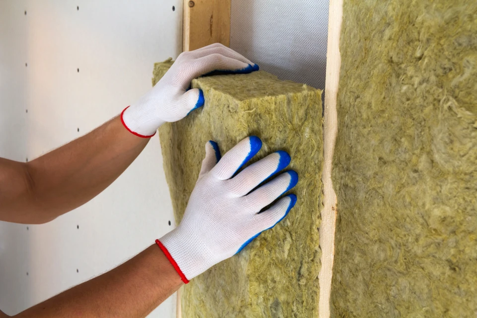 Ouvrier en gants de protection installant de l'isolant en laine minérale jaune entre montants bois dans cloison intérieure
