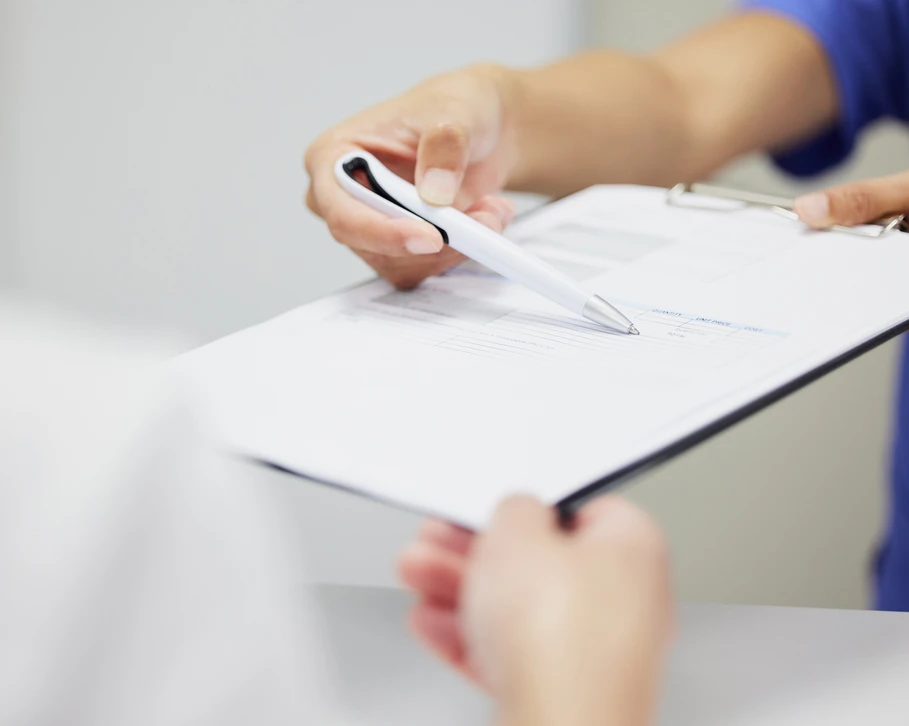 Main droite tenant un stylo &agrave; bille blanc, &eacute;crivant sur carnet &agrave; spirale ouvert pos&eacute; sur bureau en bois clair
