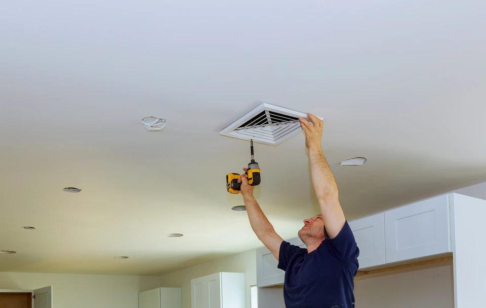 Un technicien en casque de sécurité blanc installe ou répare un système de ventilation au plafond d'un bâtiment moderne
