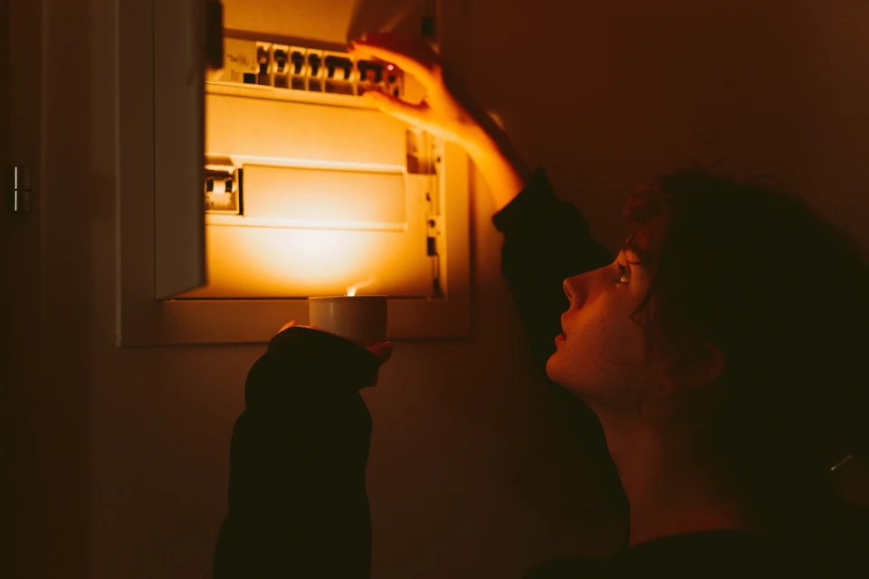 Un électricien en tenue de travail avec casque jaune effectue des mesures électriques dans un tableau de distribution résidentiel
