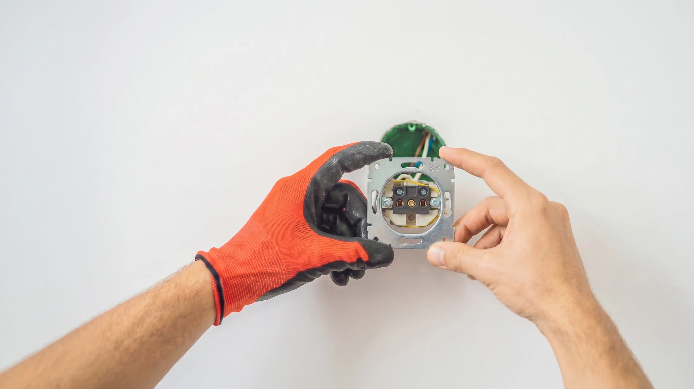 Intérieur domestique, mains d'électricien utilisant une pince à dénuder sur câbles électriques près d'un boîtier d'encastrement bleu fixé au mur blanc